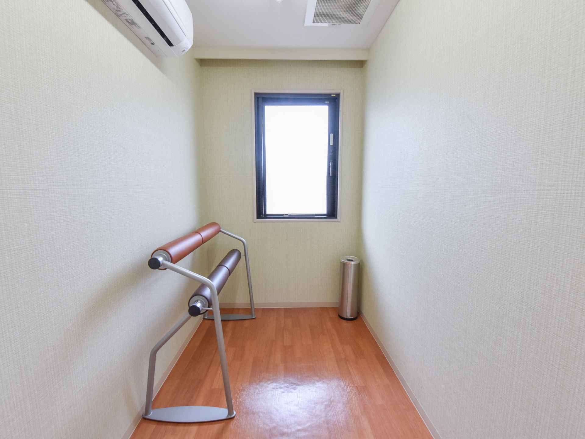 機能訓練室は全面フラットなフロアである。1方向の壁には窓が1つ設けられており、日差しが射し込んでいる。エアコンが設置されている。