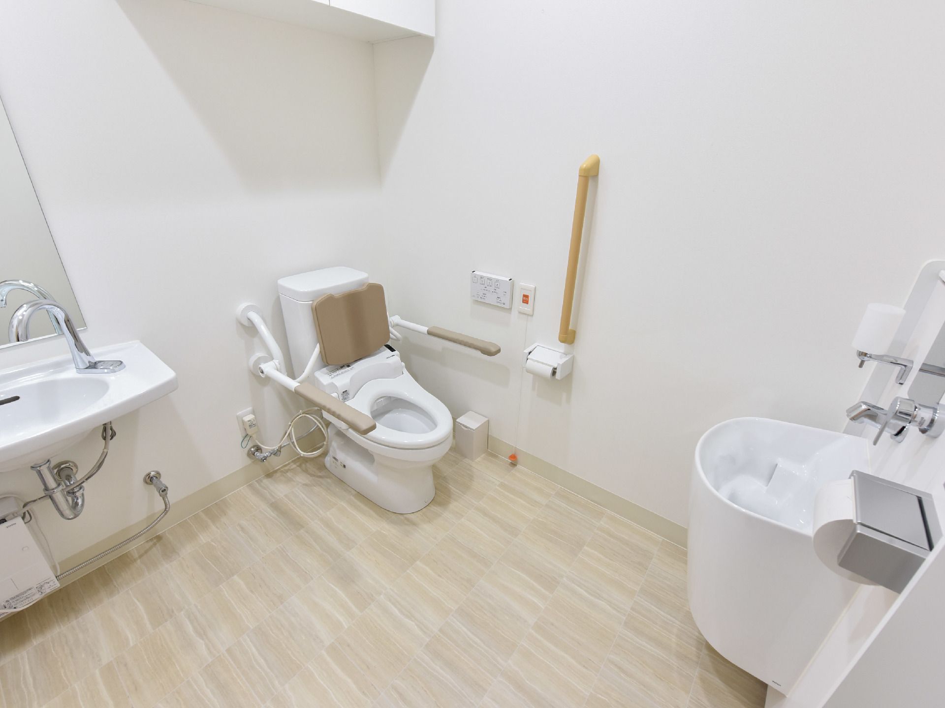 トイレと洗面はフラットなフロアにまとめられている。トイレの両脇には手すりがあり、背面には背当てパッドが取り付けられている。