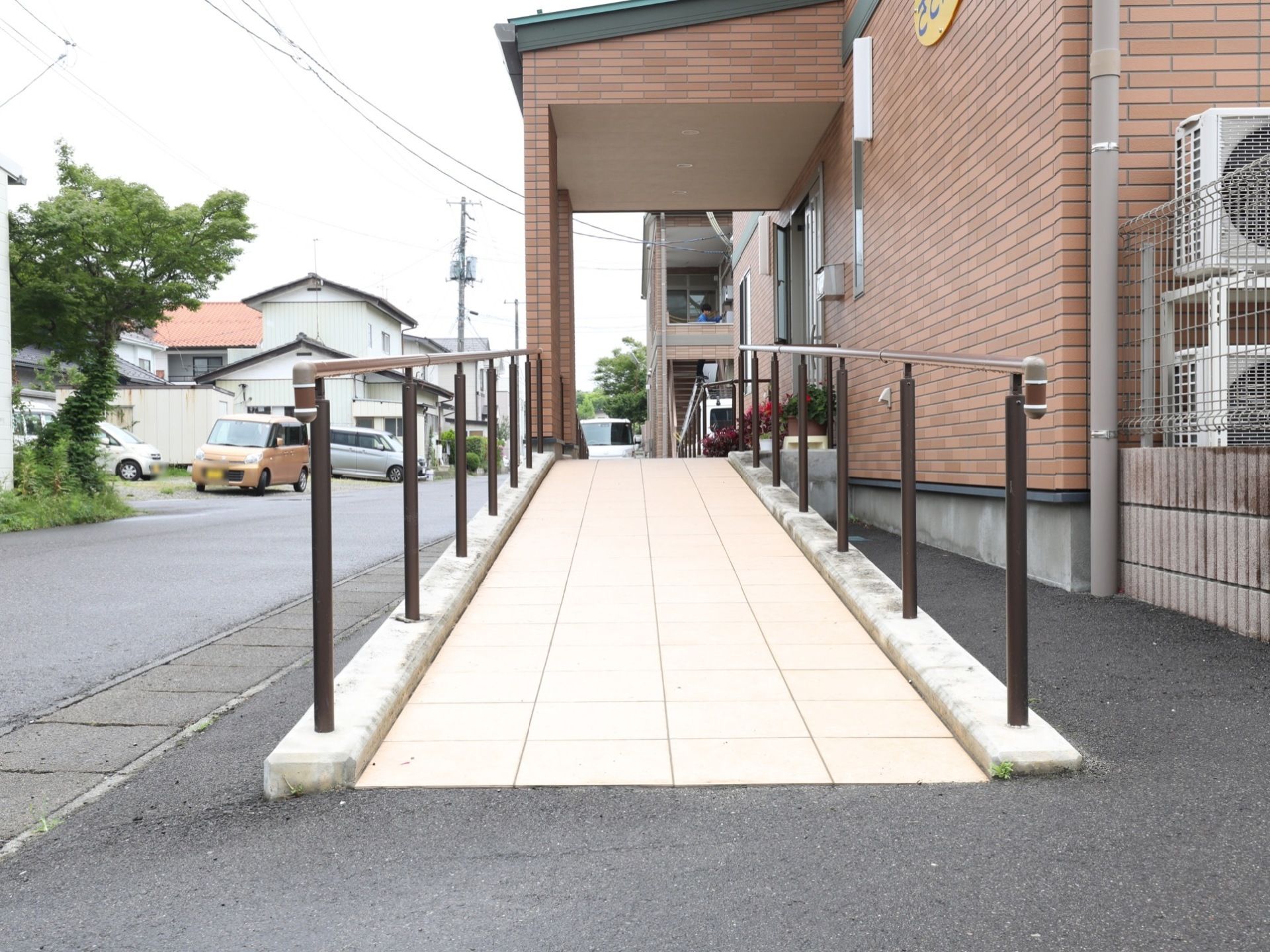 煉瓦作り外壁の施設には玄関前に続く幅の広いスロープが設置されていて、手すりも付いている。スロープ下には車が寄せられるスペースがある。