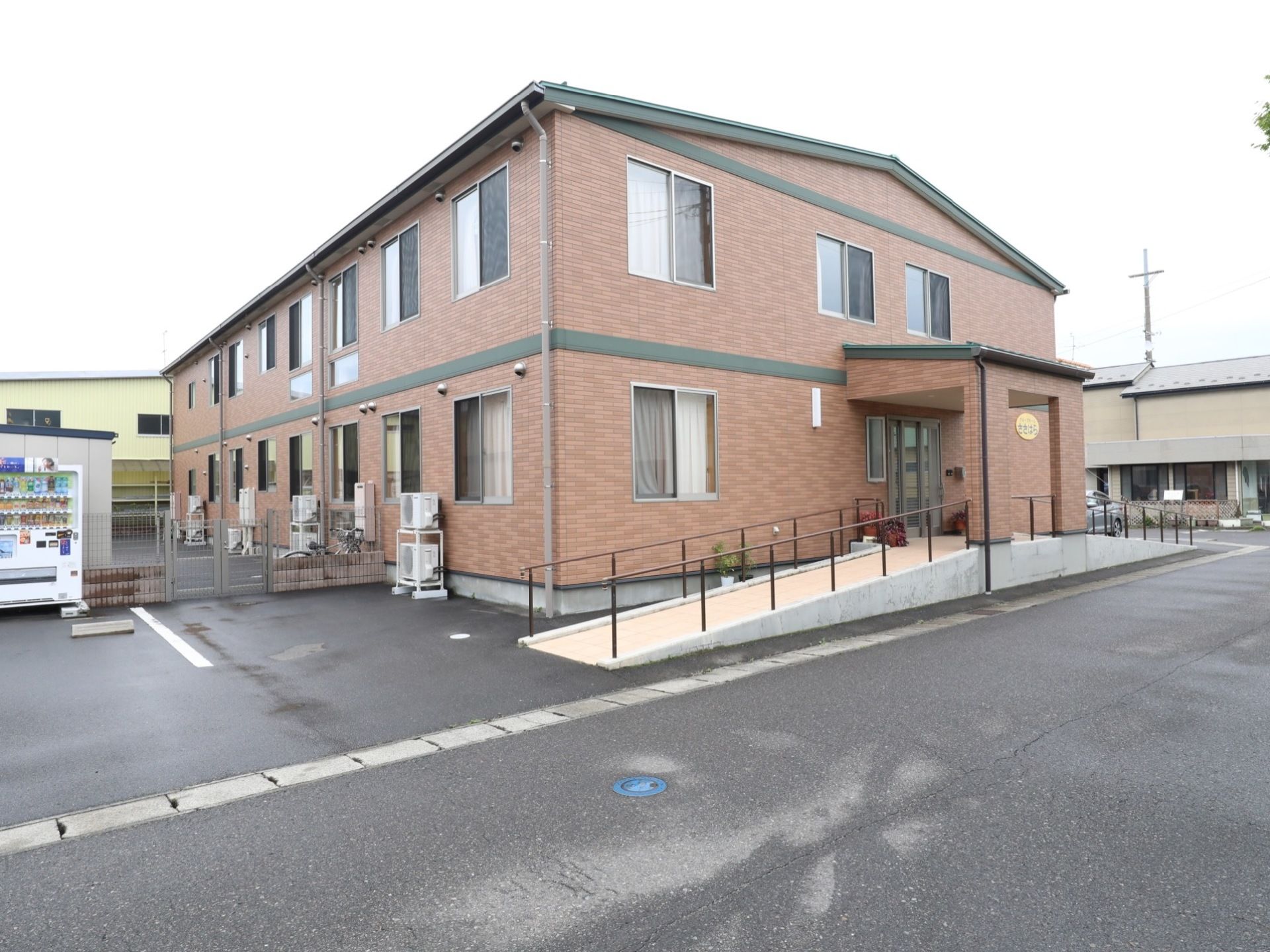 ２階建ての施設の外壁は煉瓦作りになっていて重厚感がある。玄関前には左右にスロープがある。施設前は広い道路になっている。