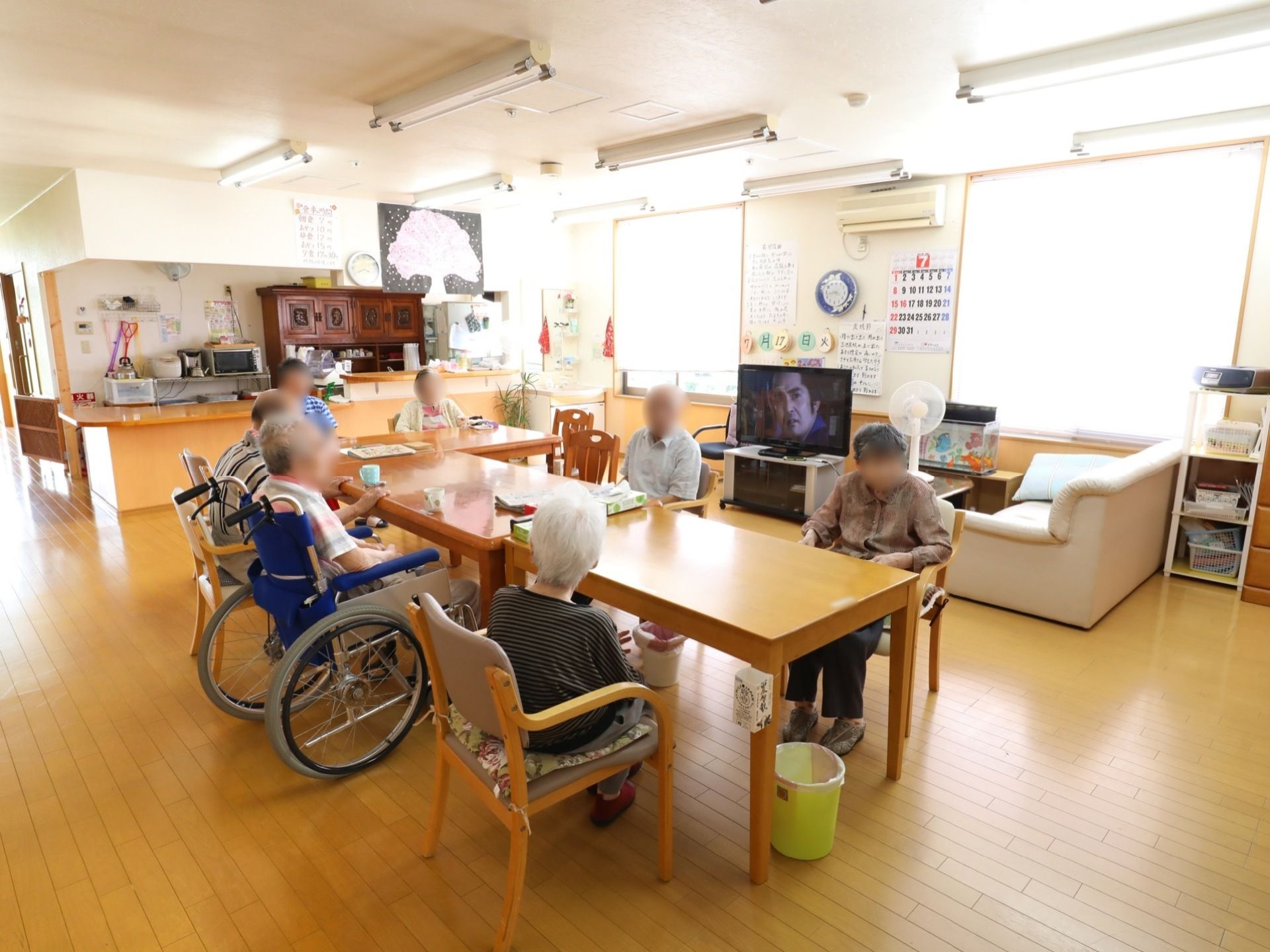 大きな窓があり明るい共有スペースである。テーブルや椅子がいくつも置かれている。エアコンやテレビも設置されている。