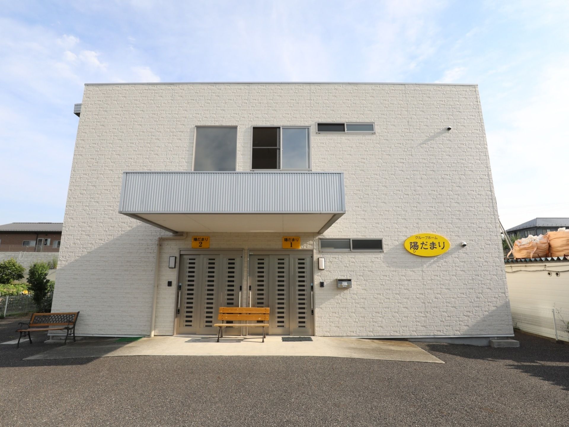 施設の建物は四角くスッキリとしたデザインである。真っ白な外壁に黄色の看板が掲げられている。出入り口付近にはベンチが設置されている。