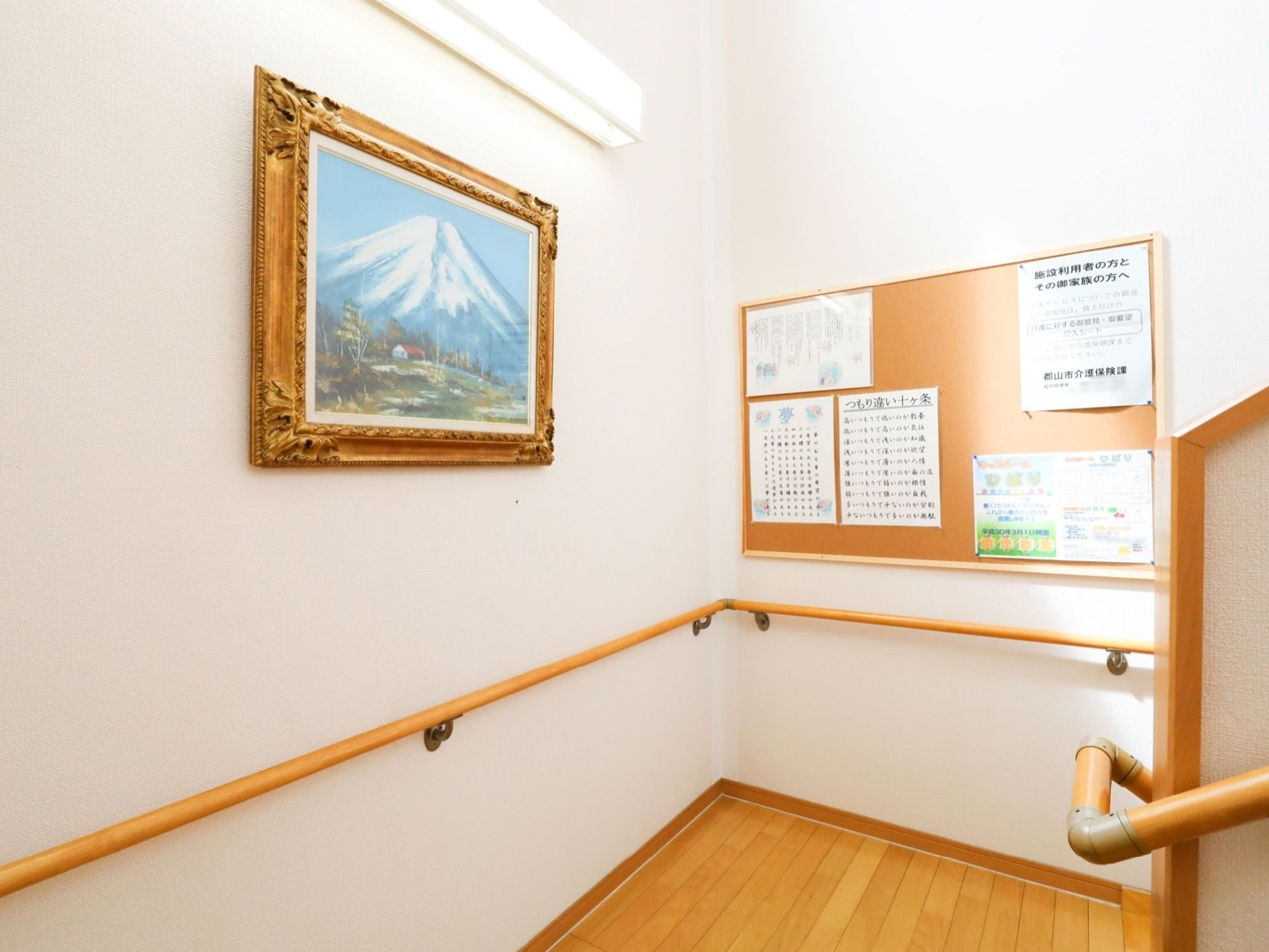 階段の踊り場の様子である。手すりが設置されていて、壁には絵画やお知らせが書かれた掲示板が備えつけられている。