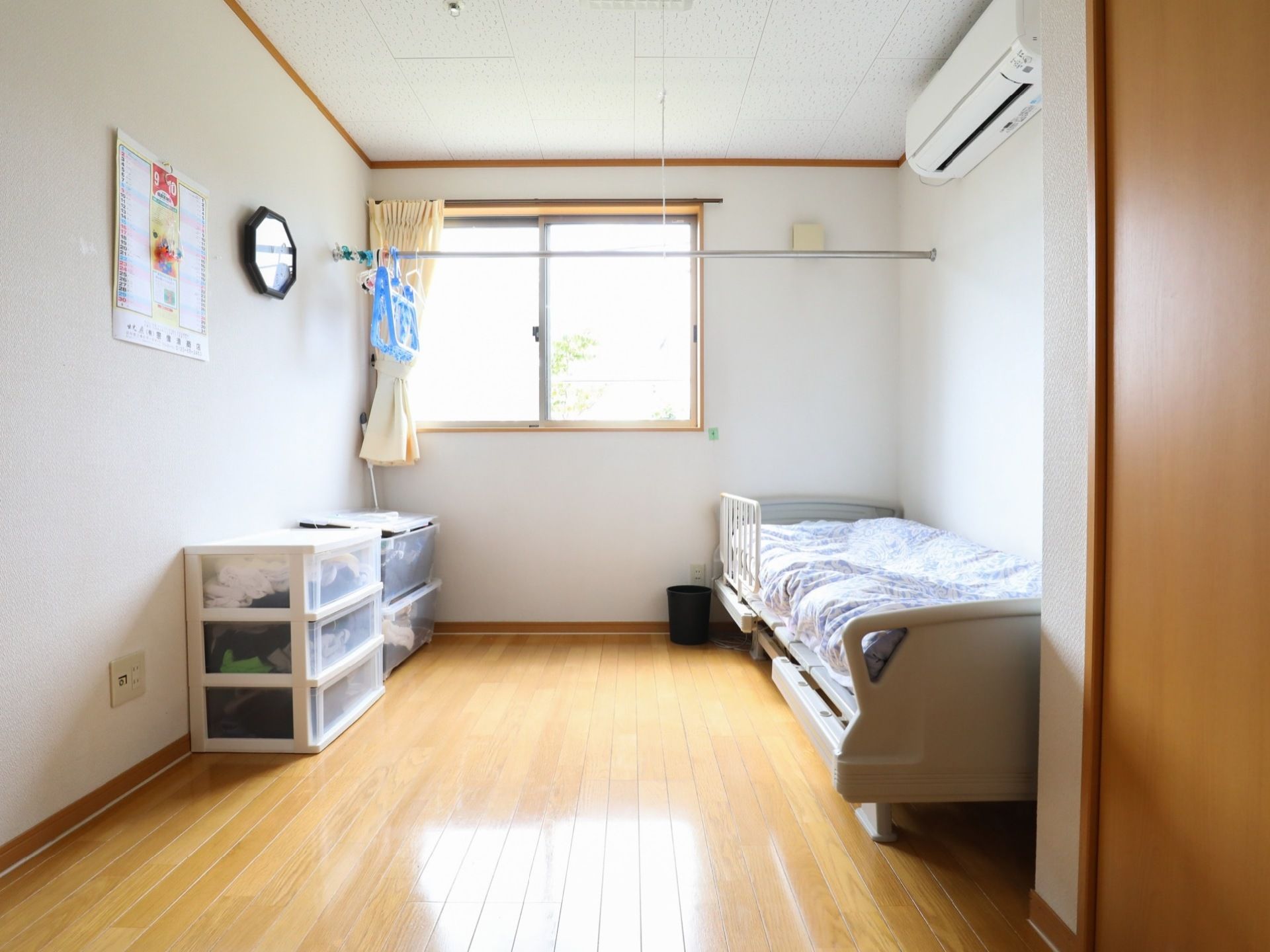 白い壁、天井に板張りの床の造りの居室である。ベッド、収納タンス、空調が完備され、物干し竿が１本設置されている。