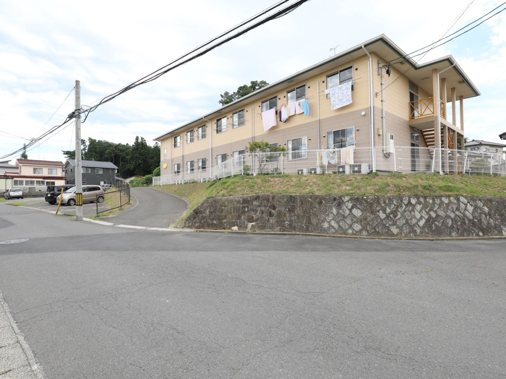 小高い角地に二階建ての建物がある。周囲は白いフェンスで囲われており、すぐ近くに駐車場がある。入口はなだらかな坂になっている。