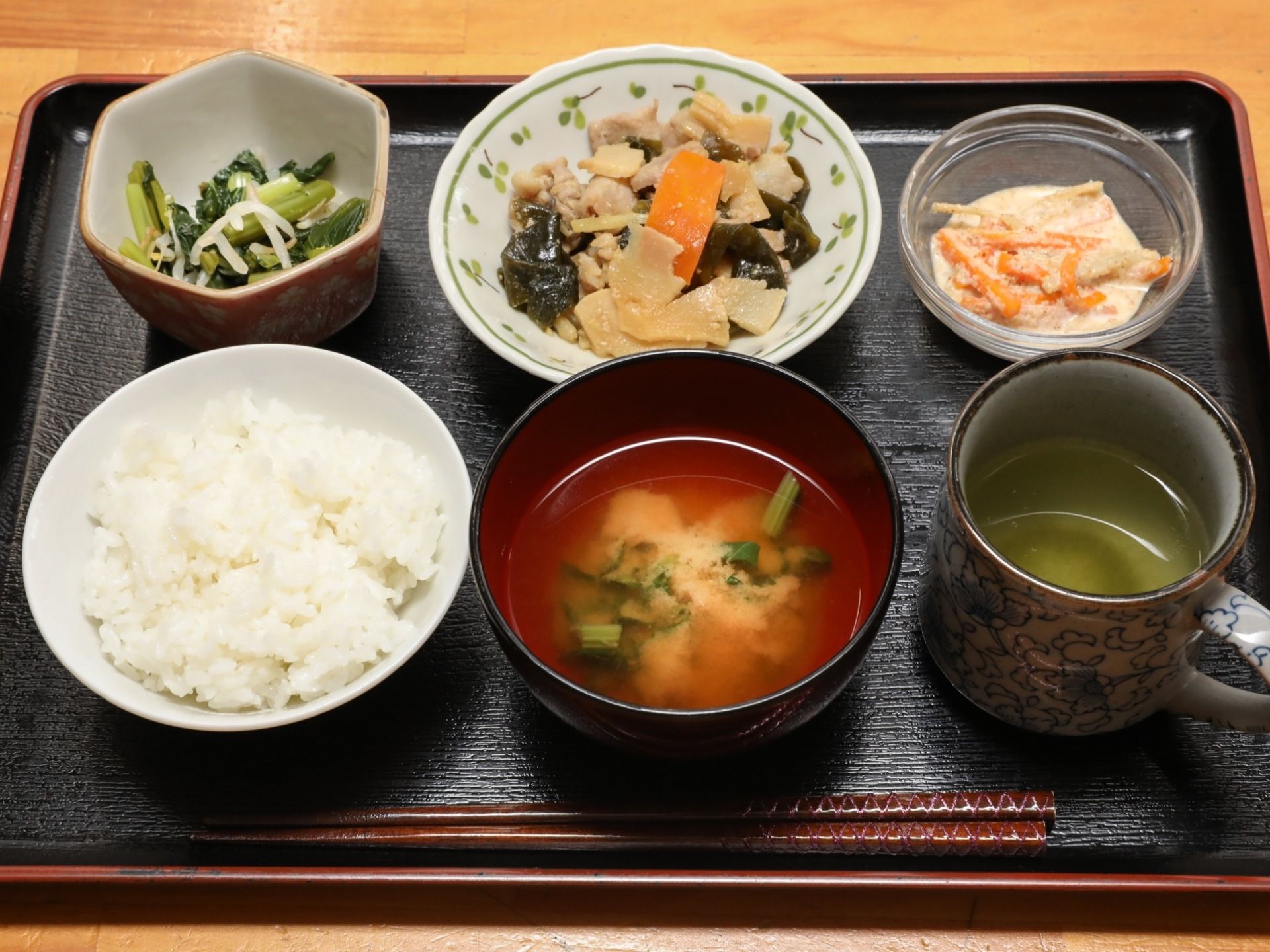 黒いトレーの上に野菜が豊富に使われた食事が置かれている。ご飯や汁物、お茶の他におかずが３品並べられている。