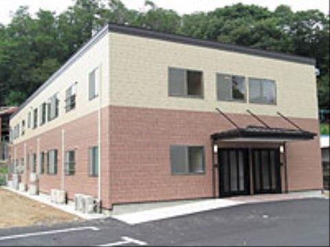 白とピンクに塗り分けられた２階建ての施設である。駐車スペースから玄関前までスロープがあり、屋根がついている。