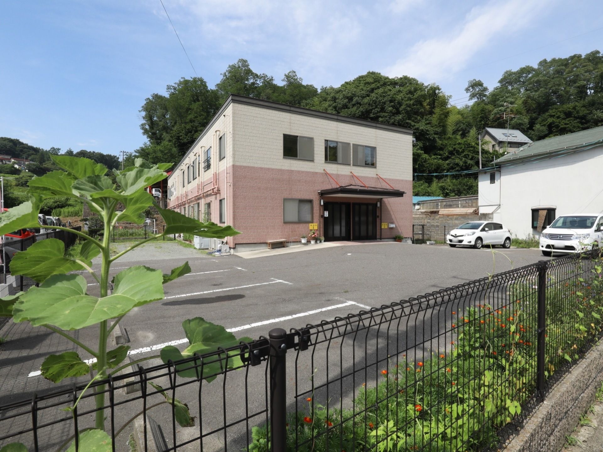 施設は二階建てで、一階部分がピンク色である。駐車場が広く、駐車が容易に行えるほか、庭も完備されている。