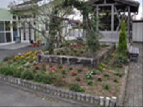 長方形の花壇が２段重ねになっている。中央にアーチ状になった緑の飾り付けがあり、周囲にさまざまな草花が植えられている。