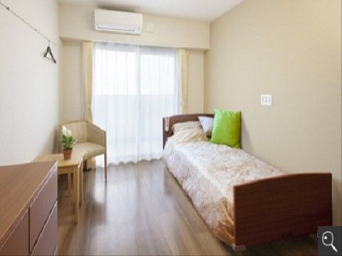 ベッド、椅子、テーブル、タンスが置かれた居室である。大きな窓から光が差し込み、明るく快適な生活を送ることができる。