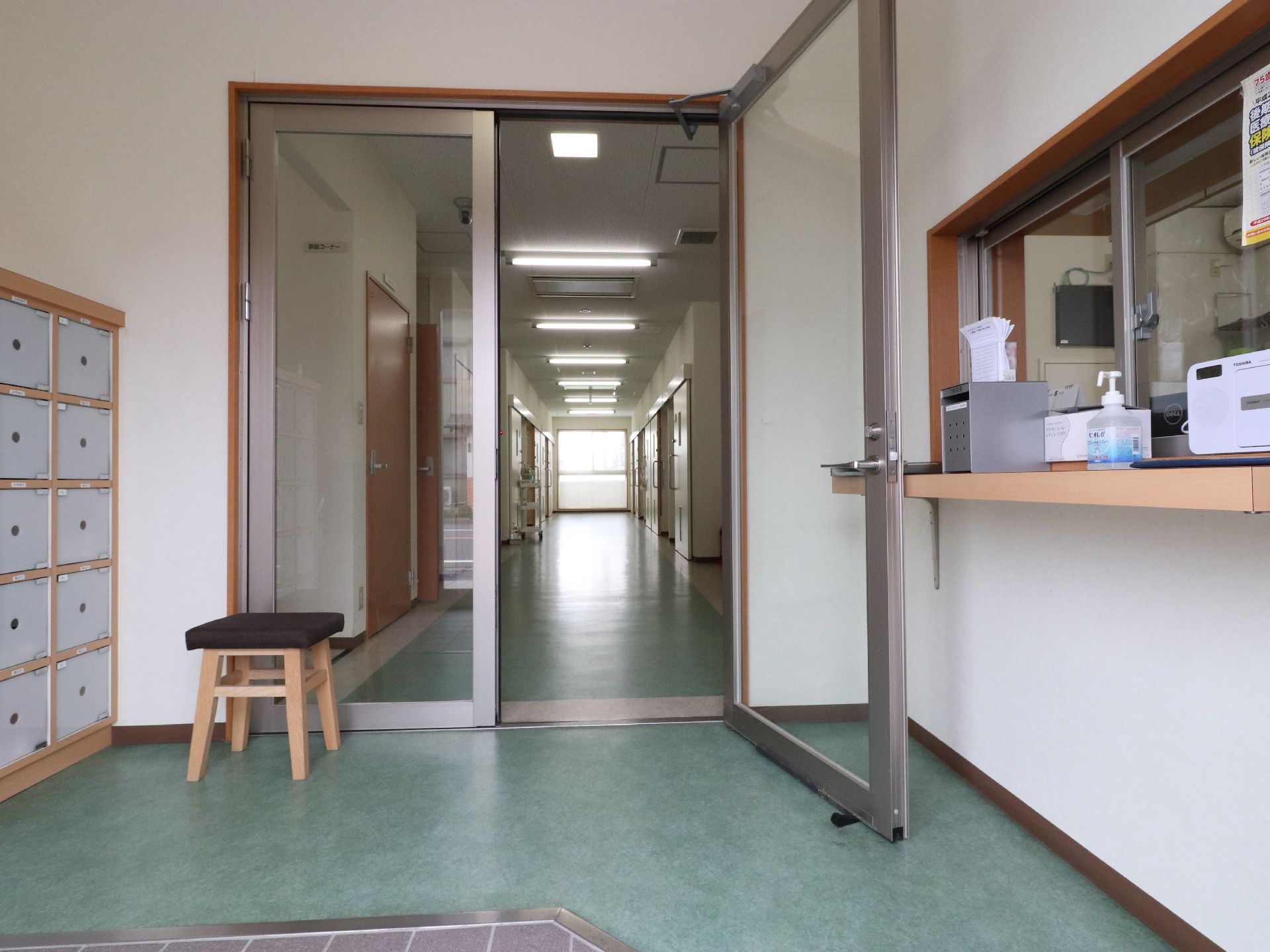 施設玄関には靴箱が設置されている。椅子が置いてあるので、靴の脱ぎ着をゆっくりと行うことができる。カウンターには消毒液などがある。