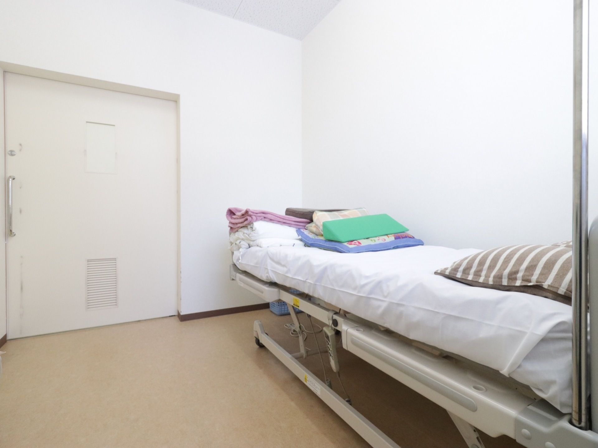 大きなスライドドアのある部屋にベッドが置かれている。清潔感のある白を基調とした部屋である。ベッドの高さは調節ができる。