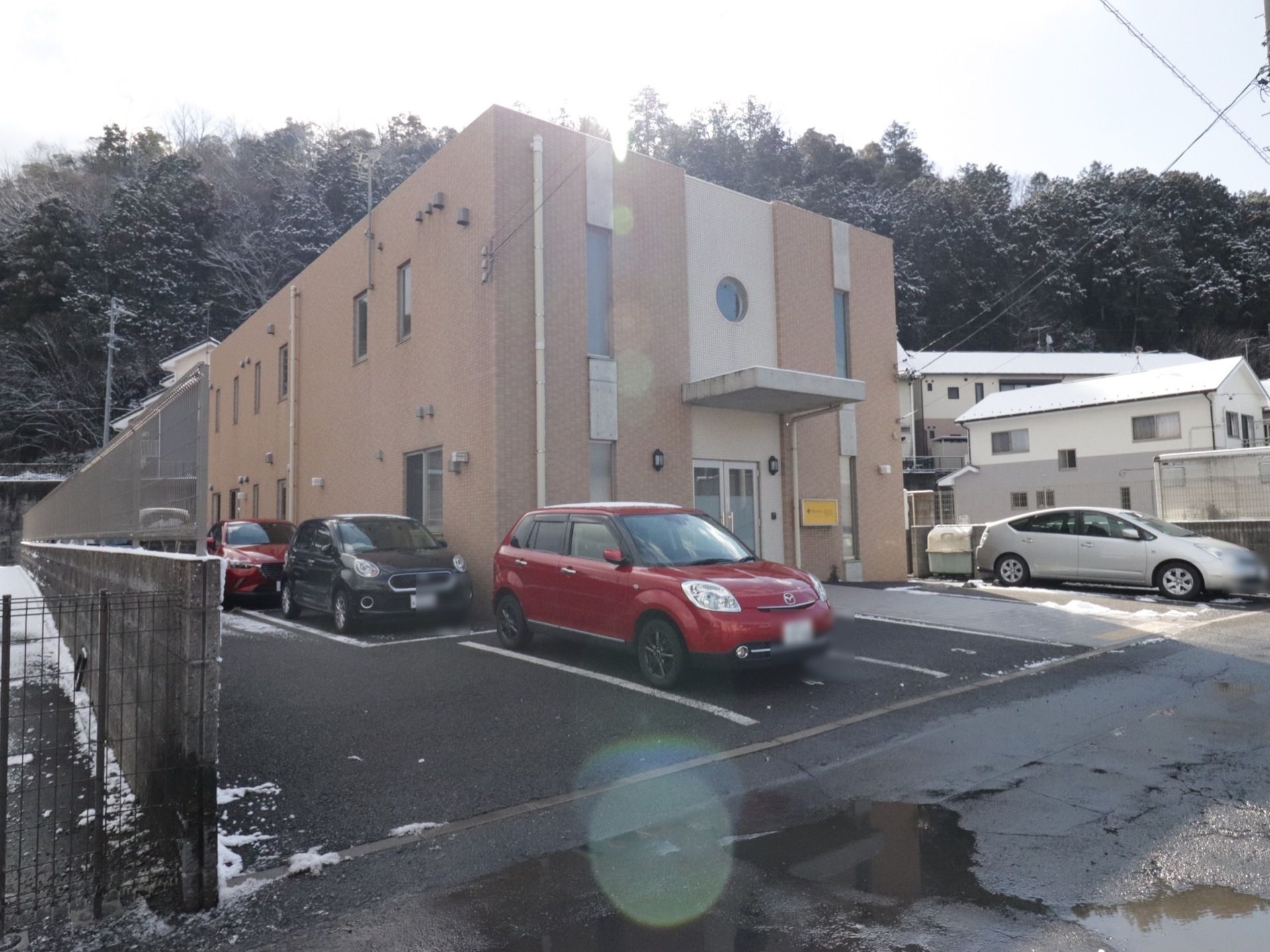 茶色と白を基調としたタイル貼りの建物である。建物裏には林がある。建物前には駐車スペースを設けている。