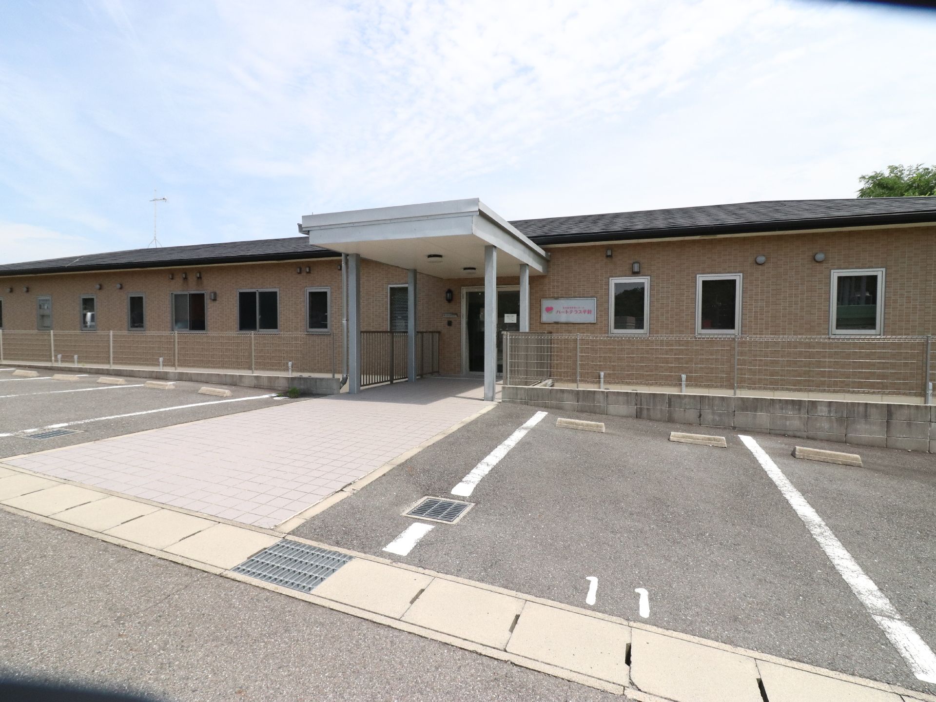 施設は平屋になっている。外観は茶色く、窓がところどころにある。入り口には屋根があり、車の駐車スペースもある。