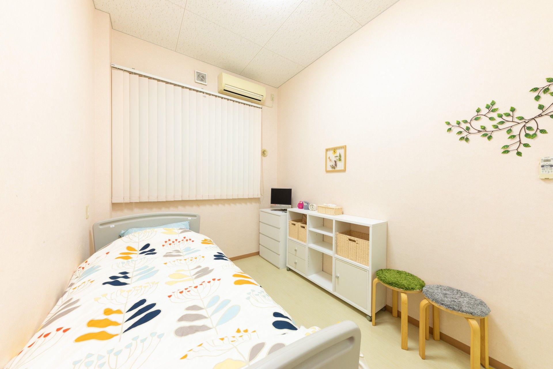小さな窓がある部屋があります。その近くにはテッシュが置かれたタンスがある。手すり付きのベッドも置かれている。