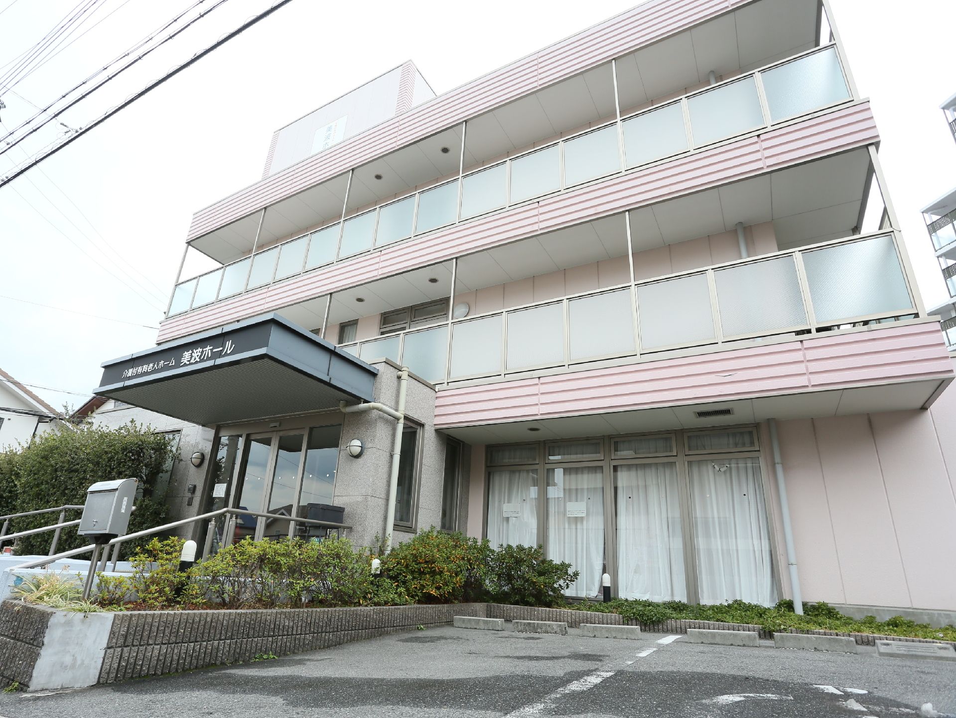 施設は３階建てである。玄関には手すりが取りつけられている。１階のガラス戸にはカーテンがかけられている。