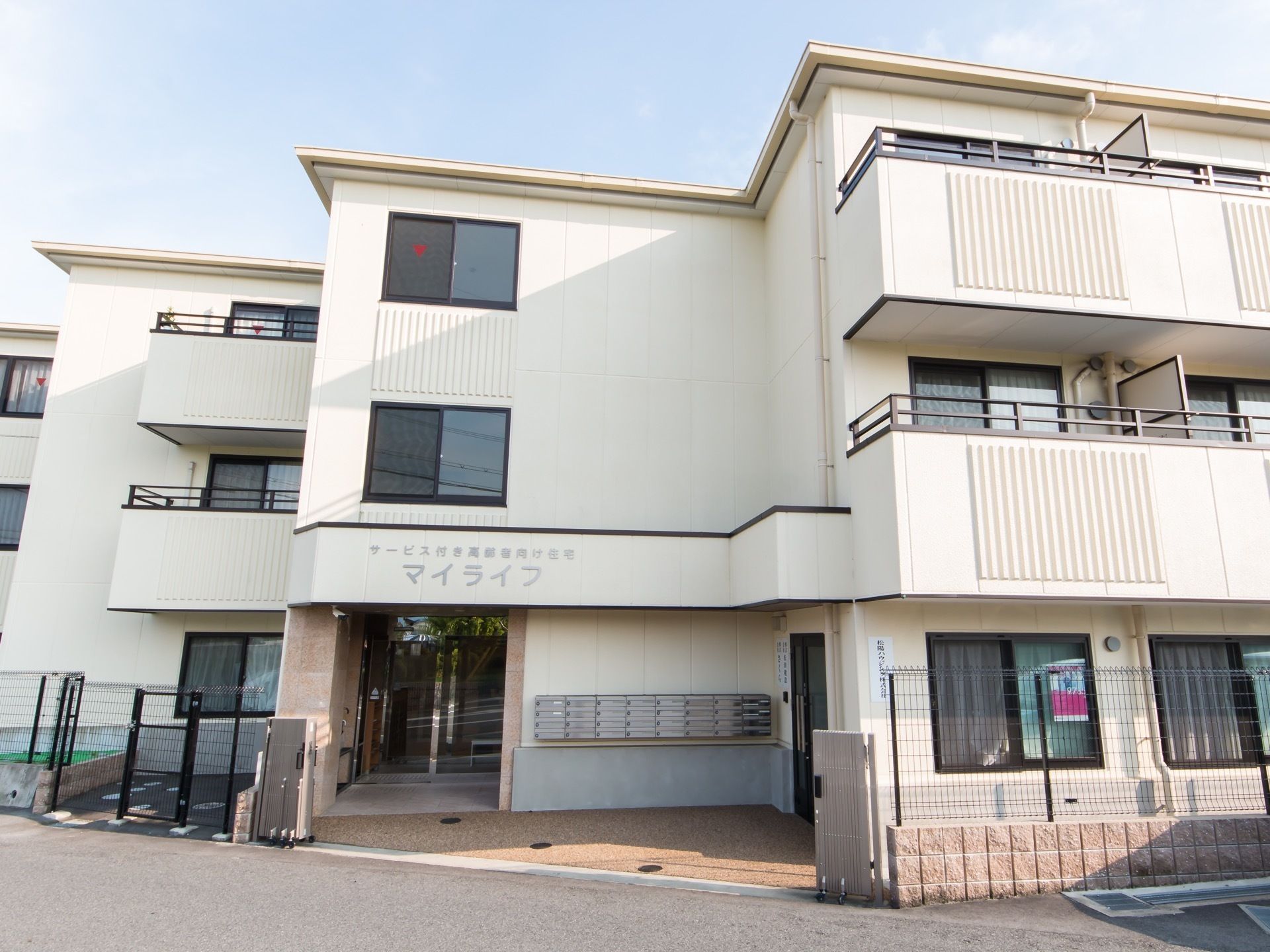 アイボリーを基調とした３階建てのおしゃれな建物である。周辺は柵で囲まれ、各居室にはバルコニーが備わっている。