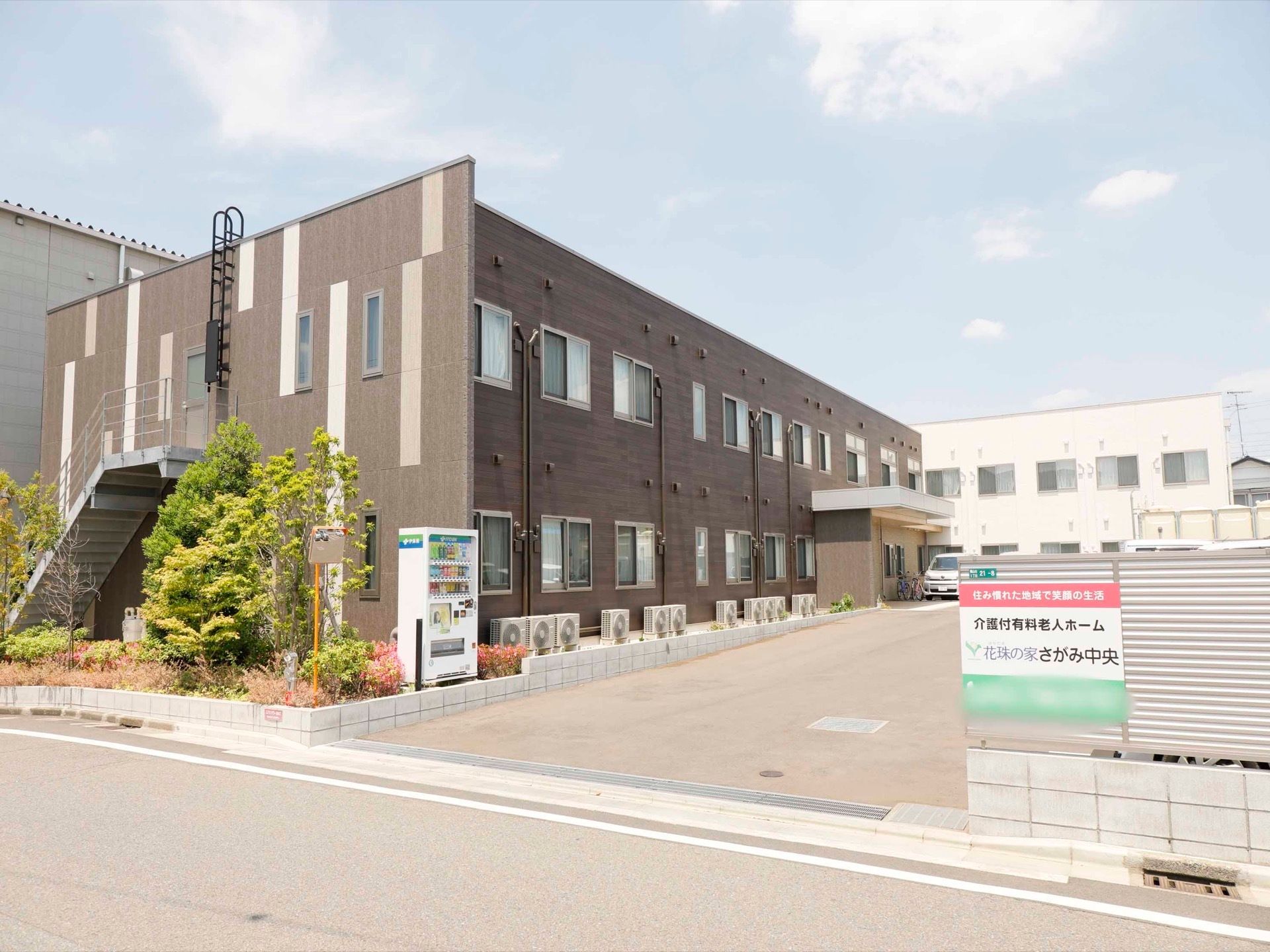 静かな環境に佇む２階建ての施設である。建物の傍に花壇を設け、中に自動販売機を備えている。敷地内の出入口の所の看板を掲げている。