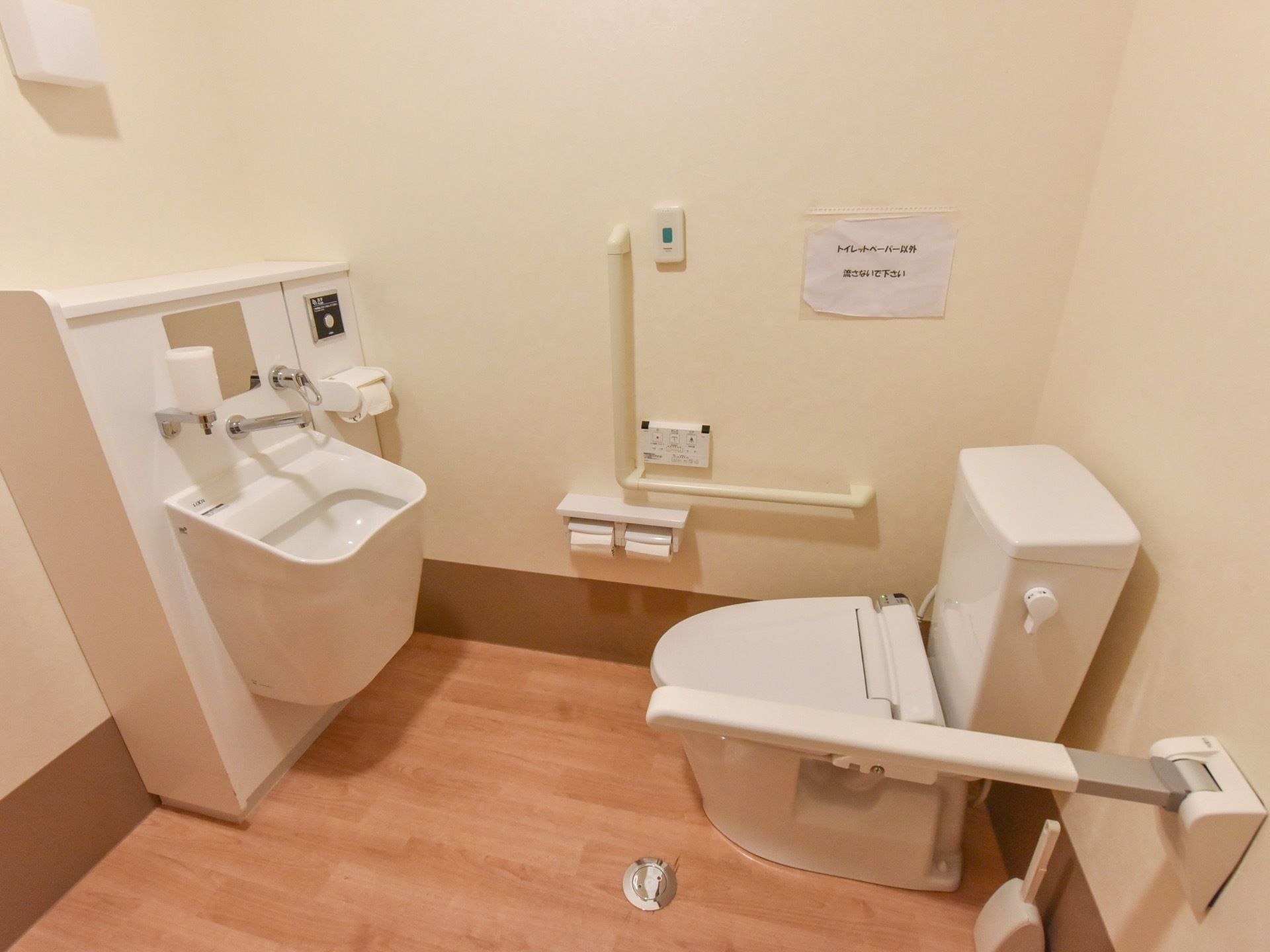 ゆったりとした木目調のフローリングのトイレスペースである。便座の両側に手すりを完備し、正面に深さのある洗面台を備えている。