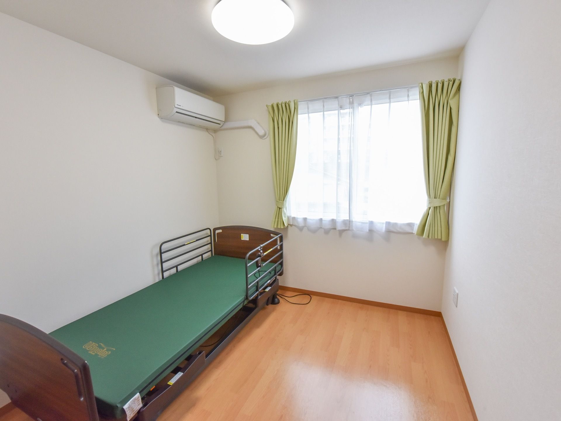 長方形の部屋の左側にベッドが置いてあり、その上には空調設備が設置されている。いくつかの家具や家電が入居者様用に用意されている。