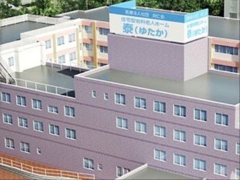 本館と新館が合わさって上から見るとコの字型になっている施設の建物。近くには緑の葉を広げる木々がある。
