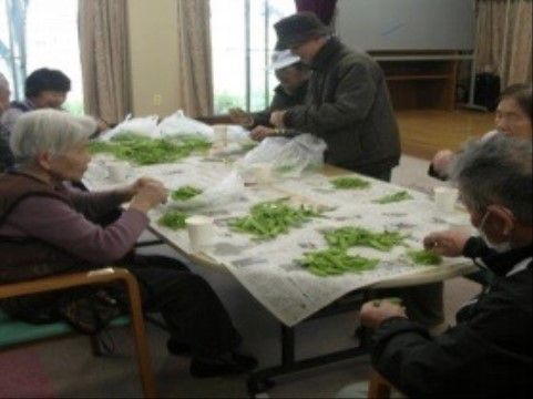 テーブルいっぱいに並べられた枝豆の下処理を手伝う入居者様