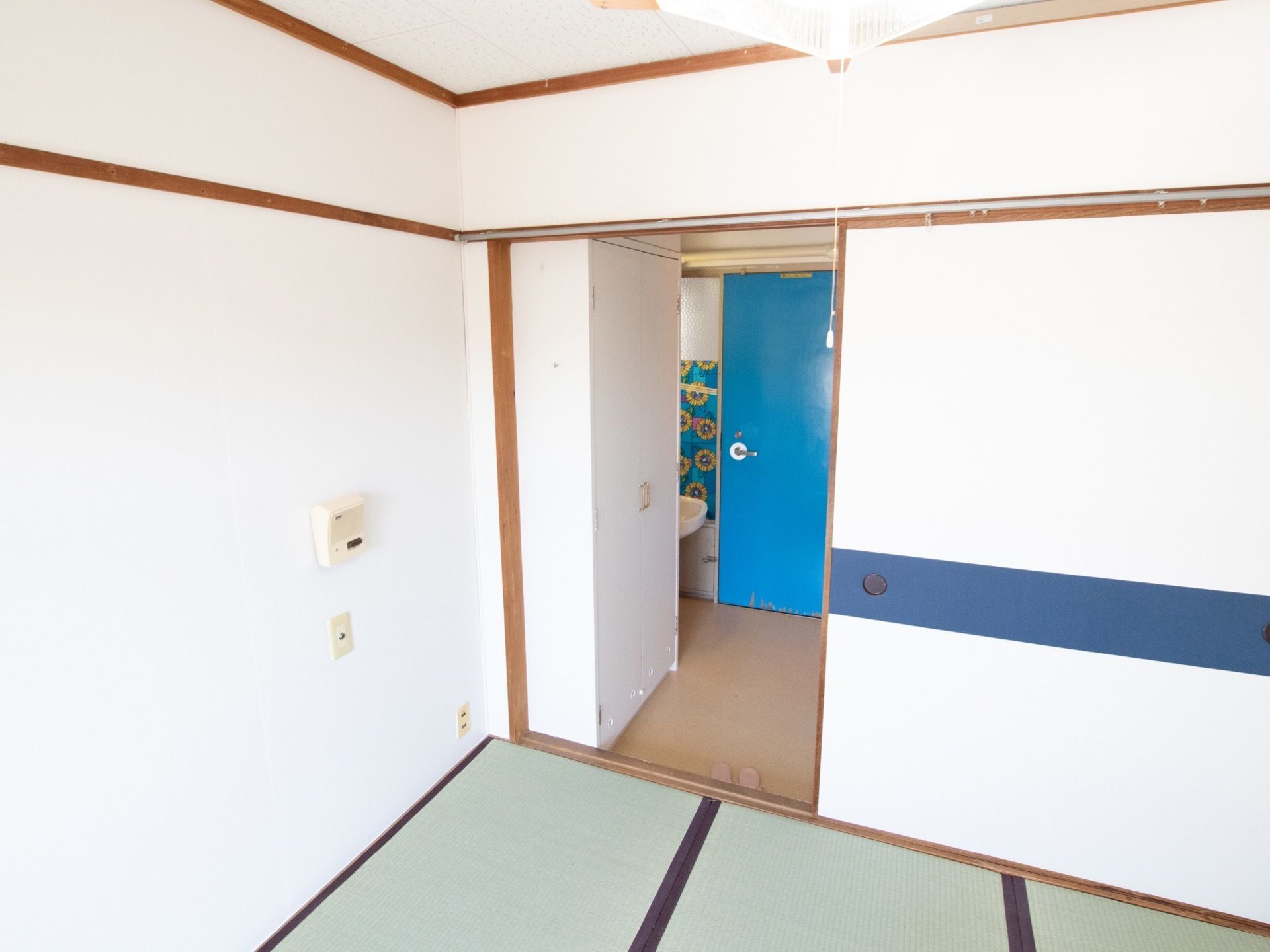 白を基調とした壁の和室。入口前には洗面所がある。大きな襖があり、和室と通路を隔てている。照明は和室向きの四角い照明が使われている。