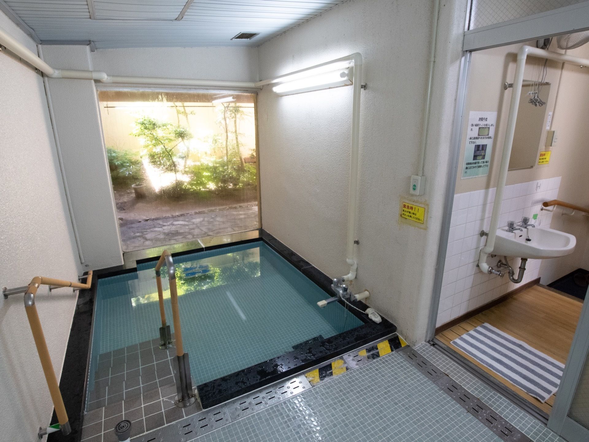 浴室には広々とした湯船が設置されている。湯船の奥が一面ガラス張りとなっていて、穏やかな日差しが降り注ぐ坪庭を望む。