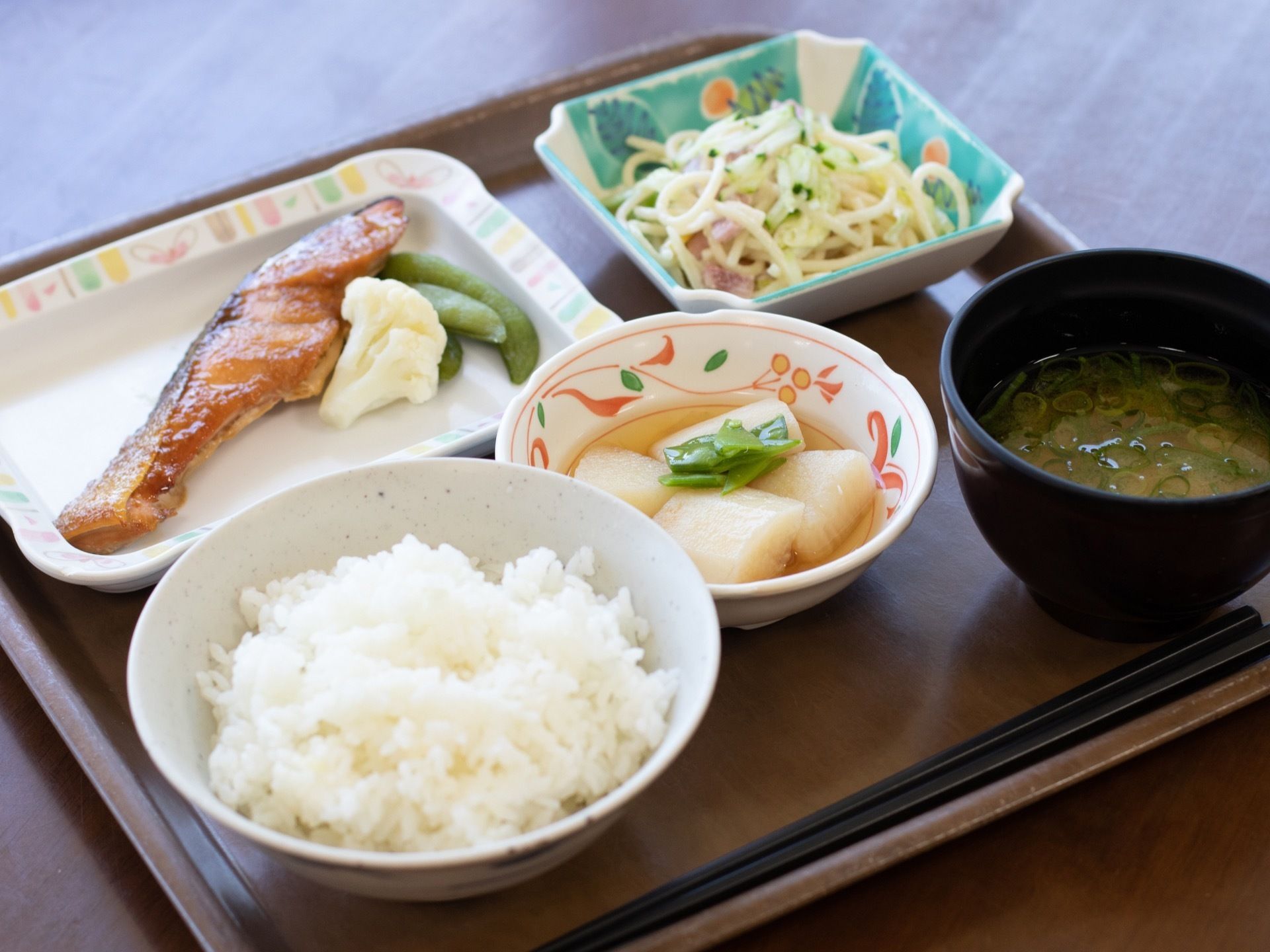 施設で出される食事である。四角いトレイに和食の献立が並んでいる。栄養バランスや彩りが考えられている。