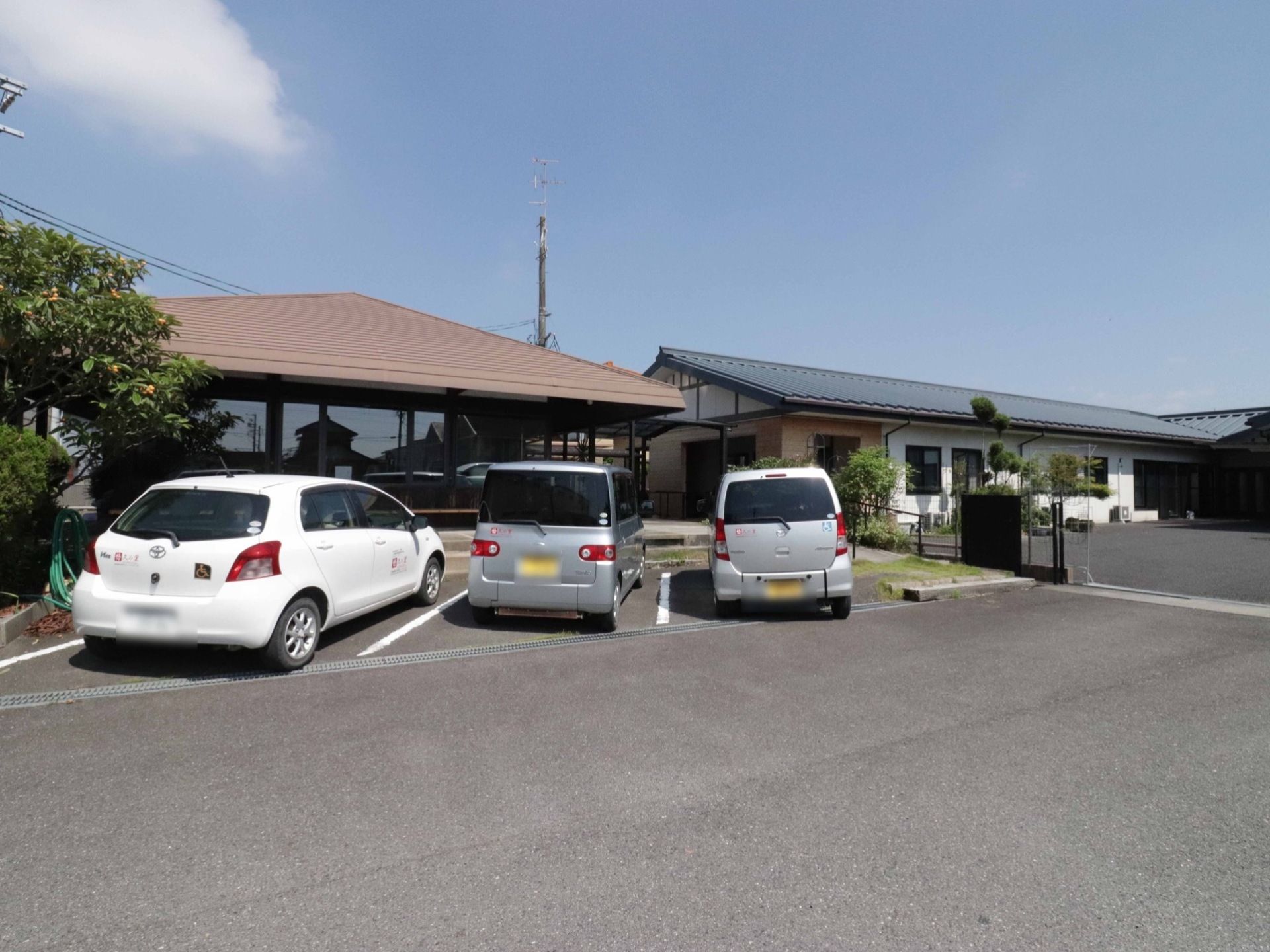 地面は舗装されており、通路も広くとってある広々とした印象がある。車が三台停まっており、樹木が植えられている。