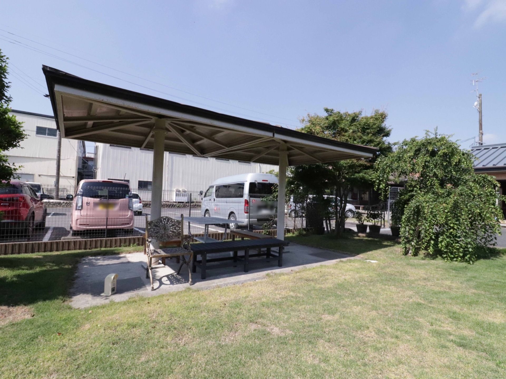 駐車場の後ろに広々とした芝生がある。いろんな種類の植物が植えられている。複数のベンチと、日差しや雨を遮るための屋根がついている。