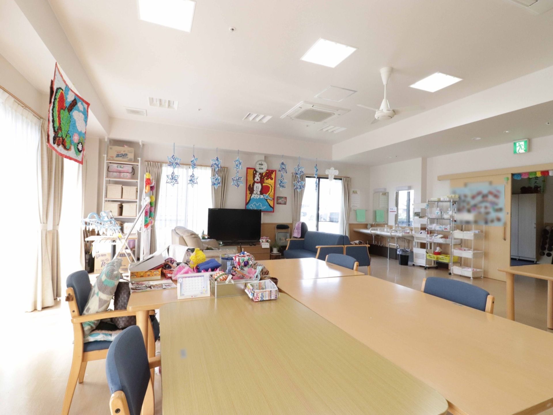 掃出し窓がいくつもある角部屋である。長いテーブルを4つ突き合わせて大きなテーブルとして使っている。エアコンは天井に埋め込まれている。