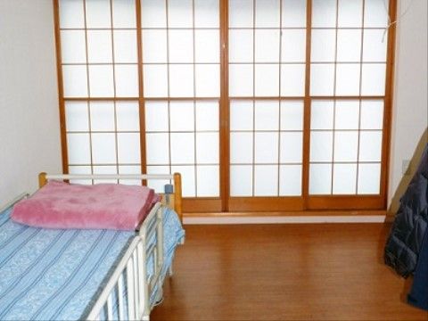 木目調のフローリングの居室のガラス張りの前方に、障子の戸を取り入れ和の空間を設けている。壁際に介護用ベッドを備えている。