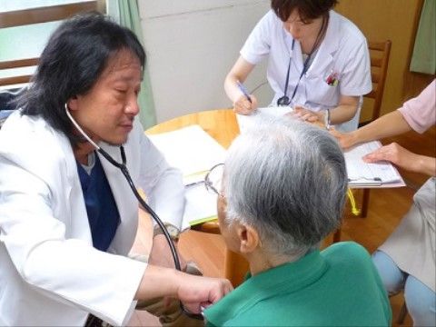 入居者様に診察を行う医師と、診察内容のメモを取る看護師や介護スタッフの様子