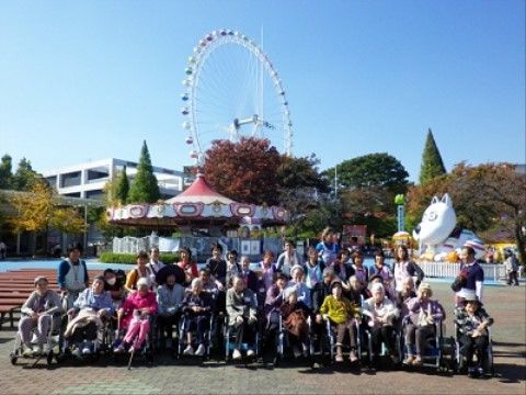 外出先の遊園地の前で集まり、楽しそうにポーズをとる入居者様とスタッフ