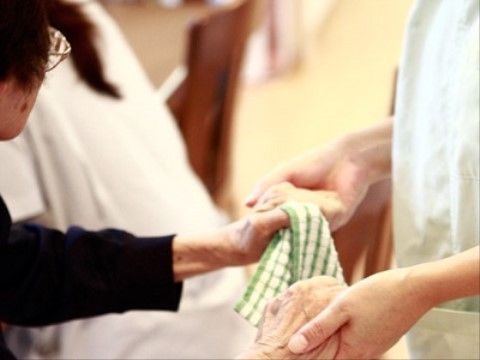 入居者様が手を伸ばし、その手を支えるようにサポートするスタッフの様子