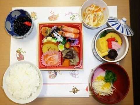 施設の食事のメニューの一例である。中央には色々なおせち料理があり、周りには鉢に入った料理のほかに、汁物のお椀とご飯が置かれている。