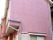 三角屋根にピンクの外壁の施設は2階建てで、一般家庭のような外観になっている。雨戸や塀は白くなっている。