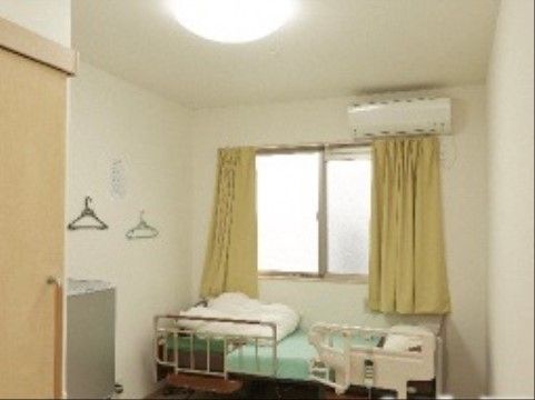大きな窓があり、広々とした居室空間。ベッドは電動で快適な生活を補助してくれる。エアコンも完備されている。