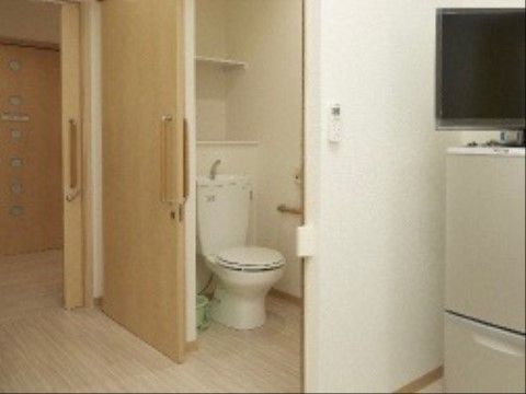 居室内のトイレの入口はスライドドアになっている。段差がないため、入居者様が安全に出入りできる。手すりが付いており、使用も楽に行える。