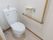 シンプルな個室トイレである。壁にはＬ字型の手すりやナースコール、ペーパーホルダーが取りつけられている。