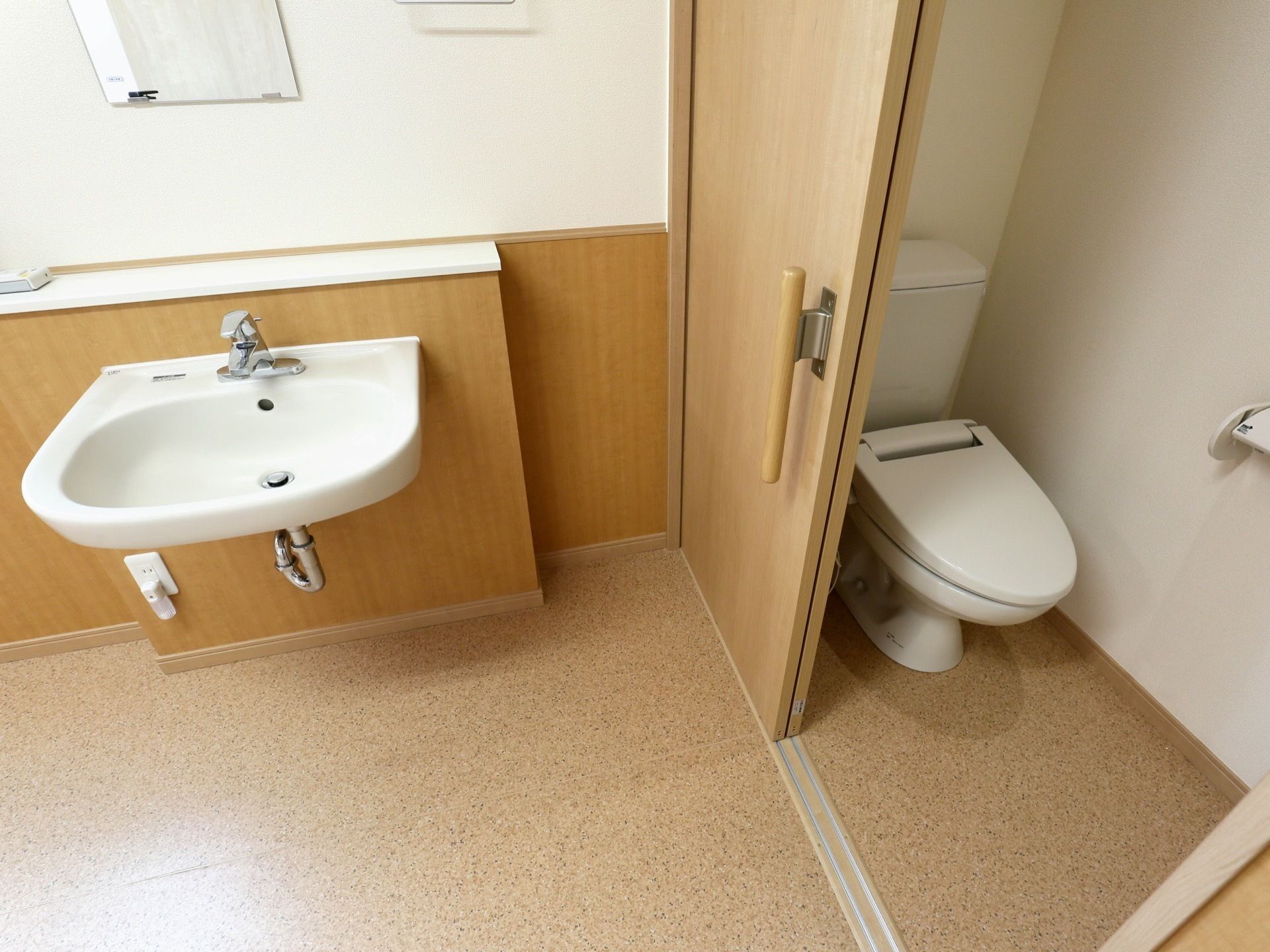 フットレス構造の洗面台があり、前方に鏡が取り付けられている。扉を挟んで洋式便座が設置されたトイレがある。