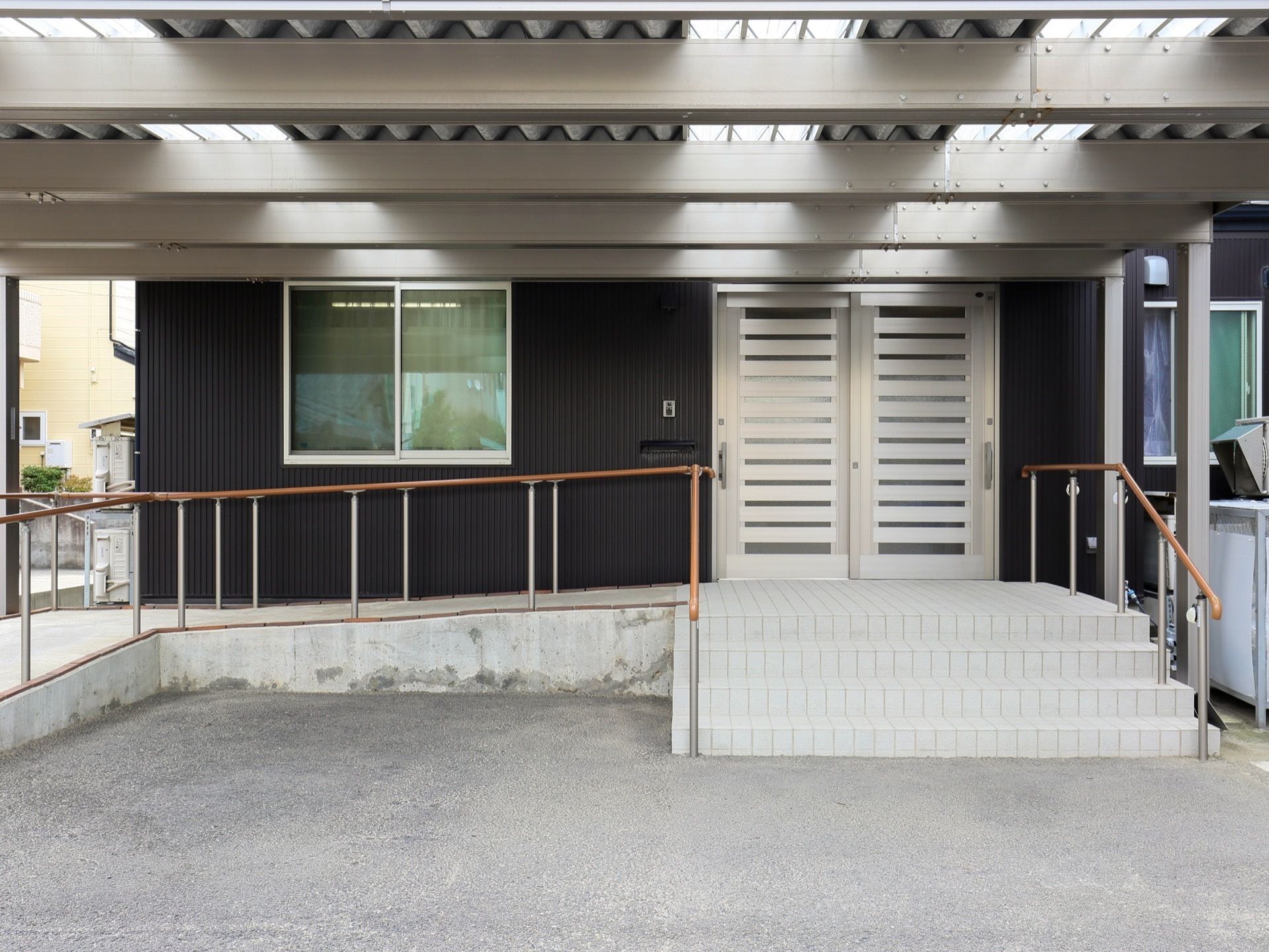 黒い外壁の建物で、玄関にはスライド式のドアが設置されている。玄関前は階段になっており、左側にスロープが設けられている。