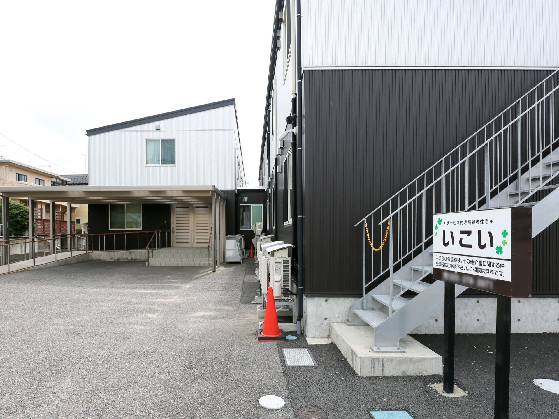 建物の横側に外階段があり、その隣に施設名が書かれた看板が建てられている。階段の登り口にはチェーンが掛けられている。