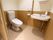 洗面台が備わった個室トイレで、壁に縦型の手すりが取り付けられている。洗面台には石鹸が1つ置かれている。