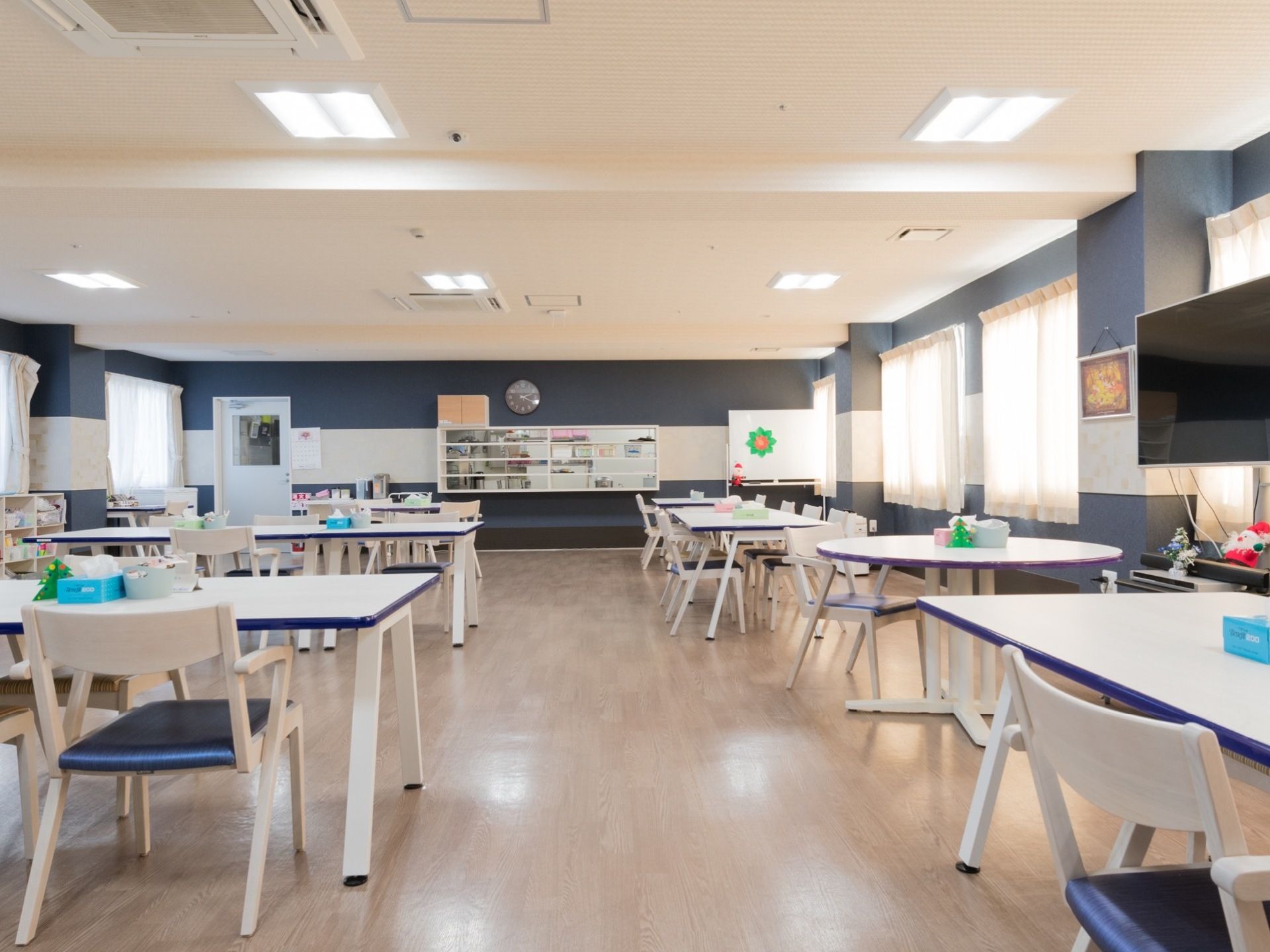 食堂と共有スペースを兼ねた広い部屋。フローリング敷きの床には白いテーブルと椅子の座席が並べられている。