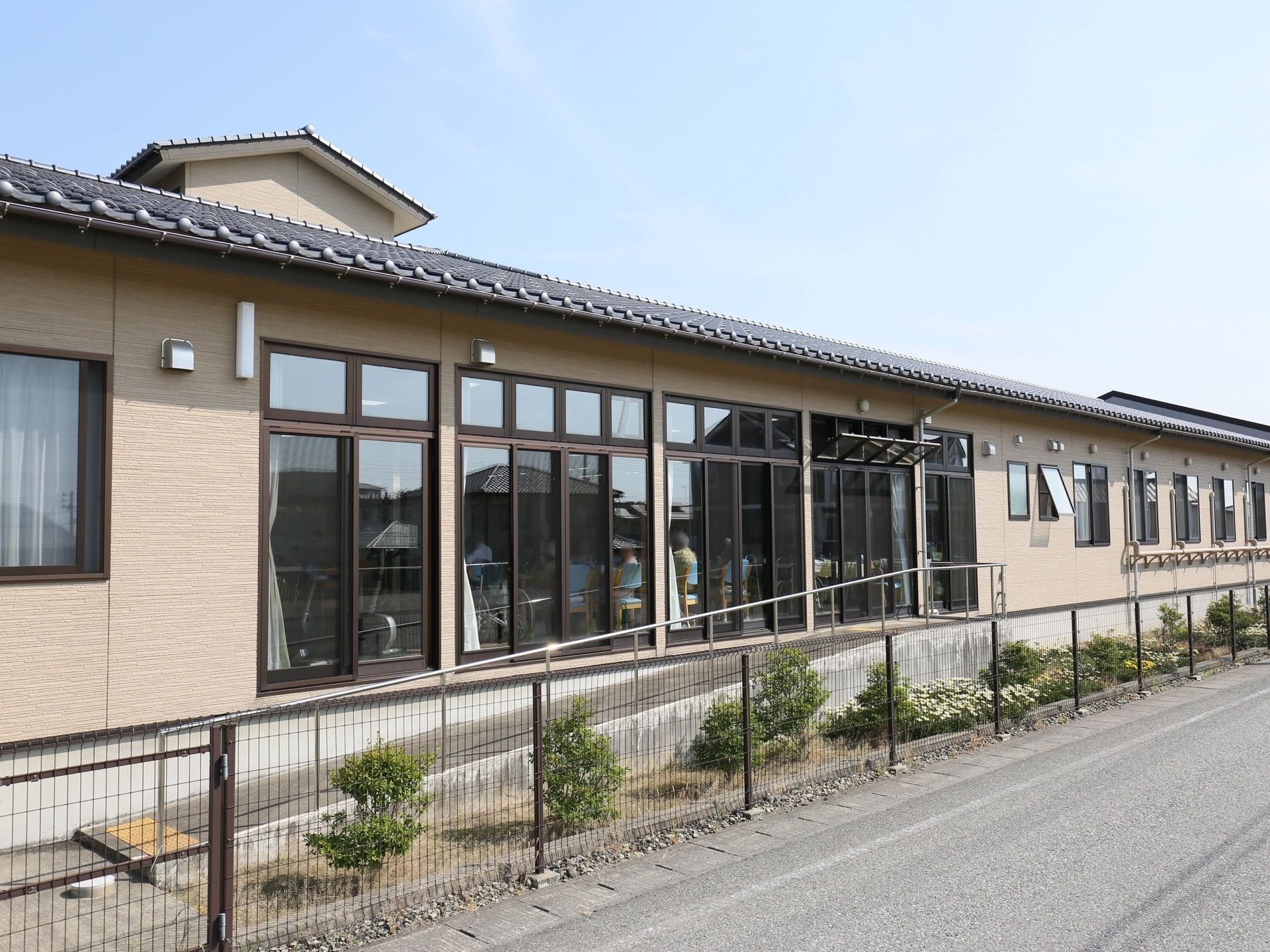 道路沿いに建っている平屋建ての施設である。上の方の小窓が外に開くようになっている。敷地境界にはフェンスが設置されている。