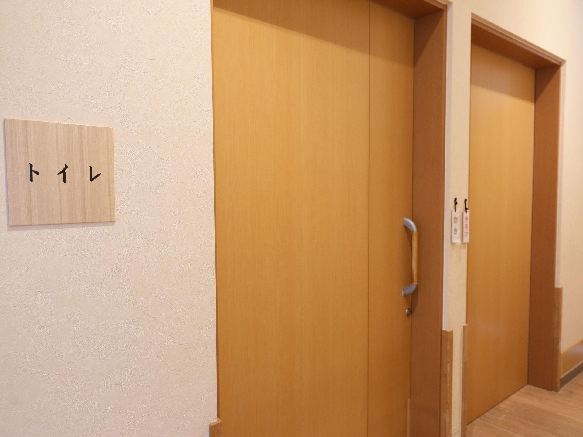 共同トイレの入口は、大きな取っ手のついた引き戸である。扉の左側の壁に、トイレ表示板が貼り付けられている。