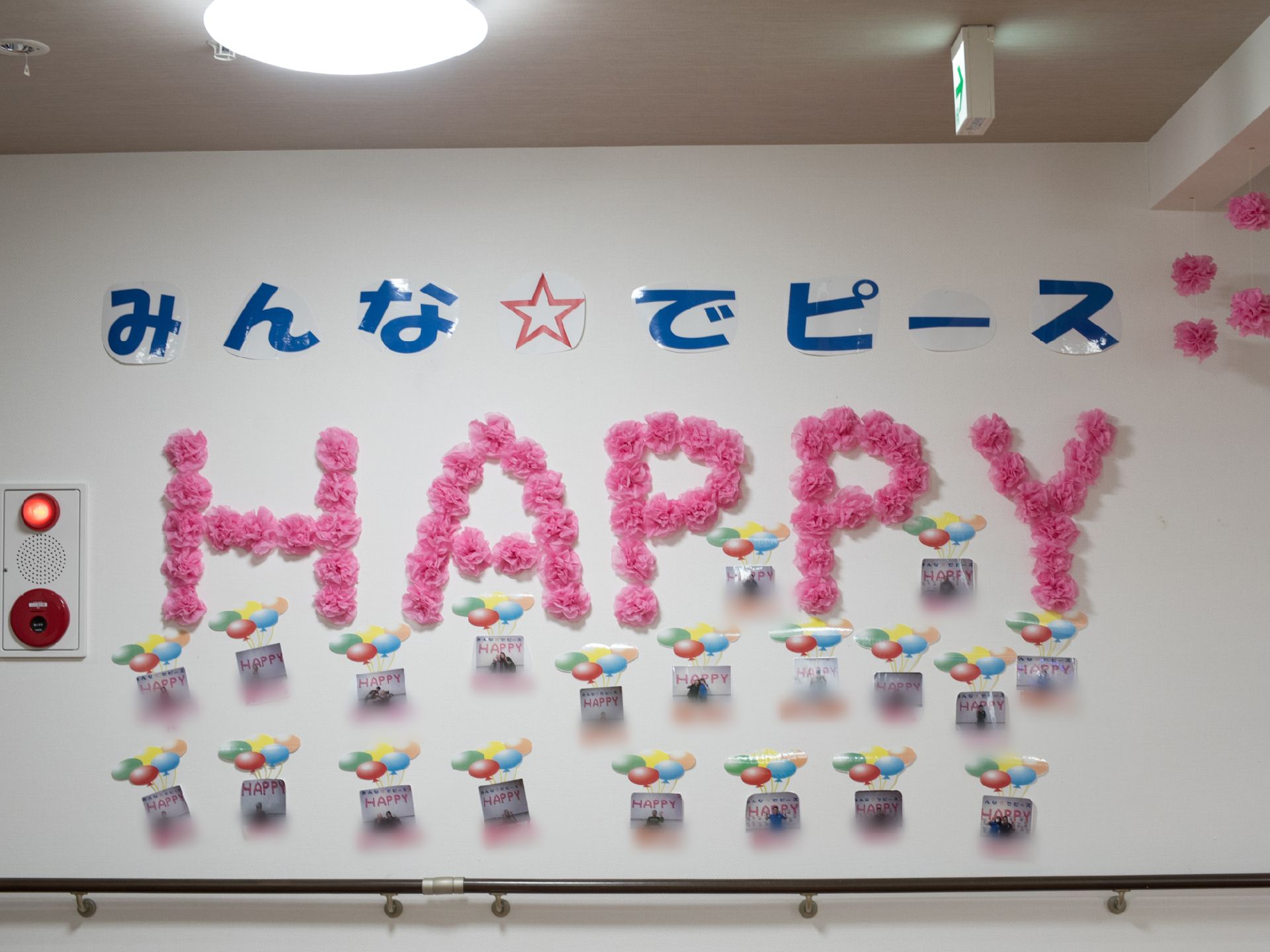 施設の壁に、HAPPYと紙の花を文字に見立てたデコレーションが施されている。様々な色が白い壁を彩っている。