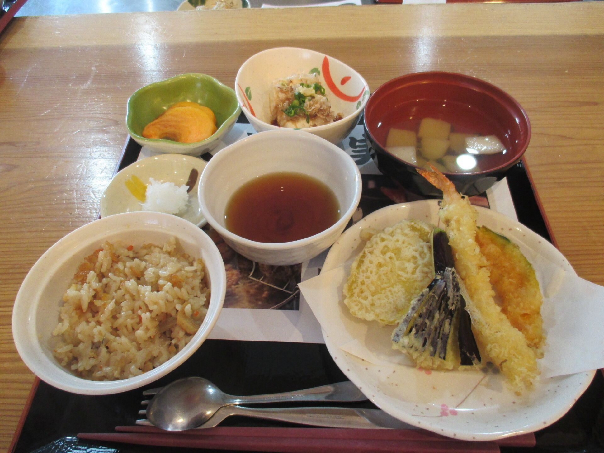 ご飯とみそ汁のほかに、焼き魚を主菜としたおかずが４皿、お盆に置かれている。手前には、スプーンが添えられている。